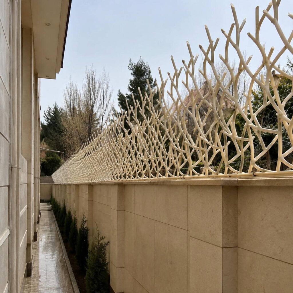 نرده سرنیزه‌ای آهنی با رنگ طوسی روی دیوار آجری